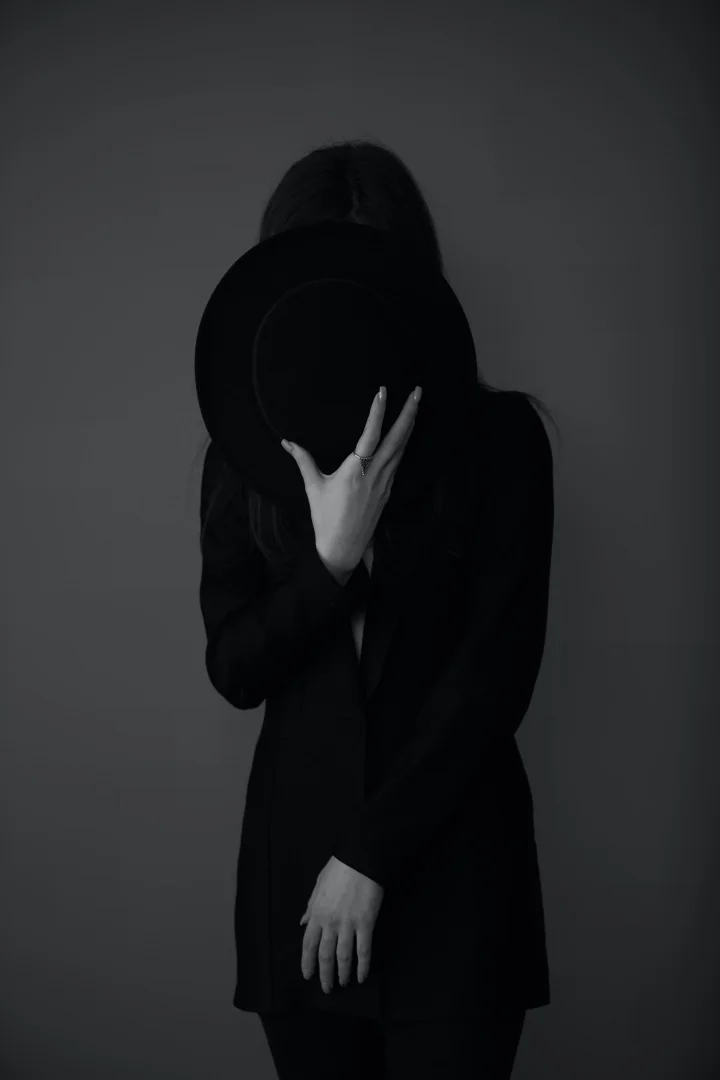 Person in black hiding their face behind a wide-brimmed hat