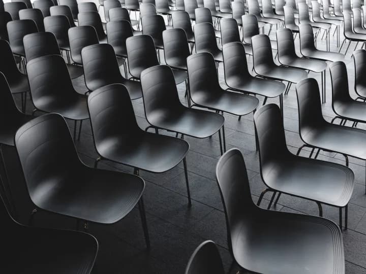Rows of empty black chairs in an auditorium